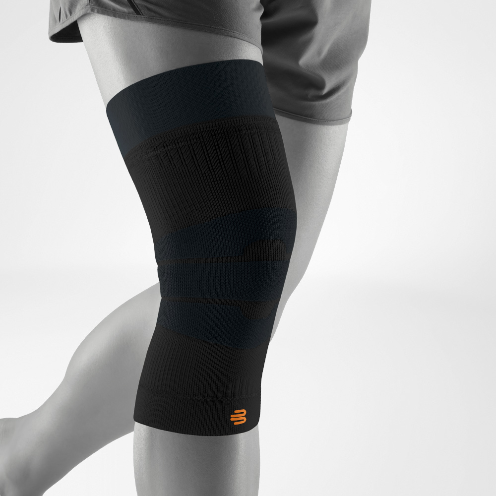 Black knee support in side view worn on the leg. The flexible compression knit supports the joint during outdoor activities such as running, hiking, or training.