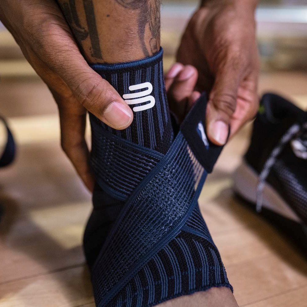 Step by step stability. Alt-Text: Close-up of a black ankle support with integrated support zones and an elastic strap for individual adjustment.
