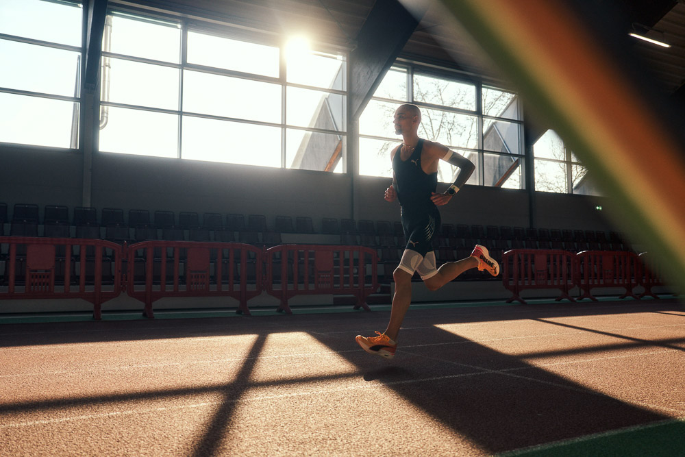 Marathon runner Hendrik Pfeiffer trains on an indoor track in backlight, wearing compression arm and leg sleeves for stability and performance.