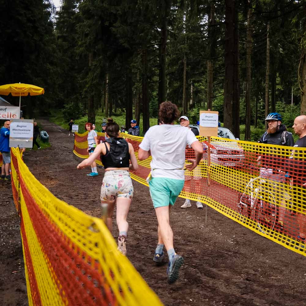 A man and a woman walk through the forest, watched by passers-by, while the ground is muddy