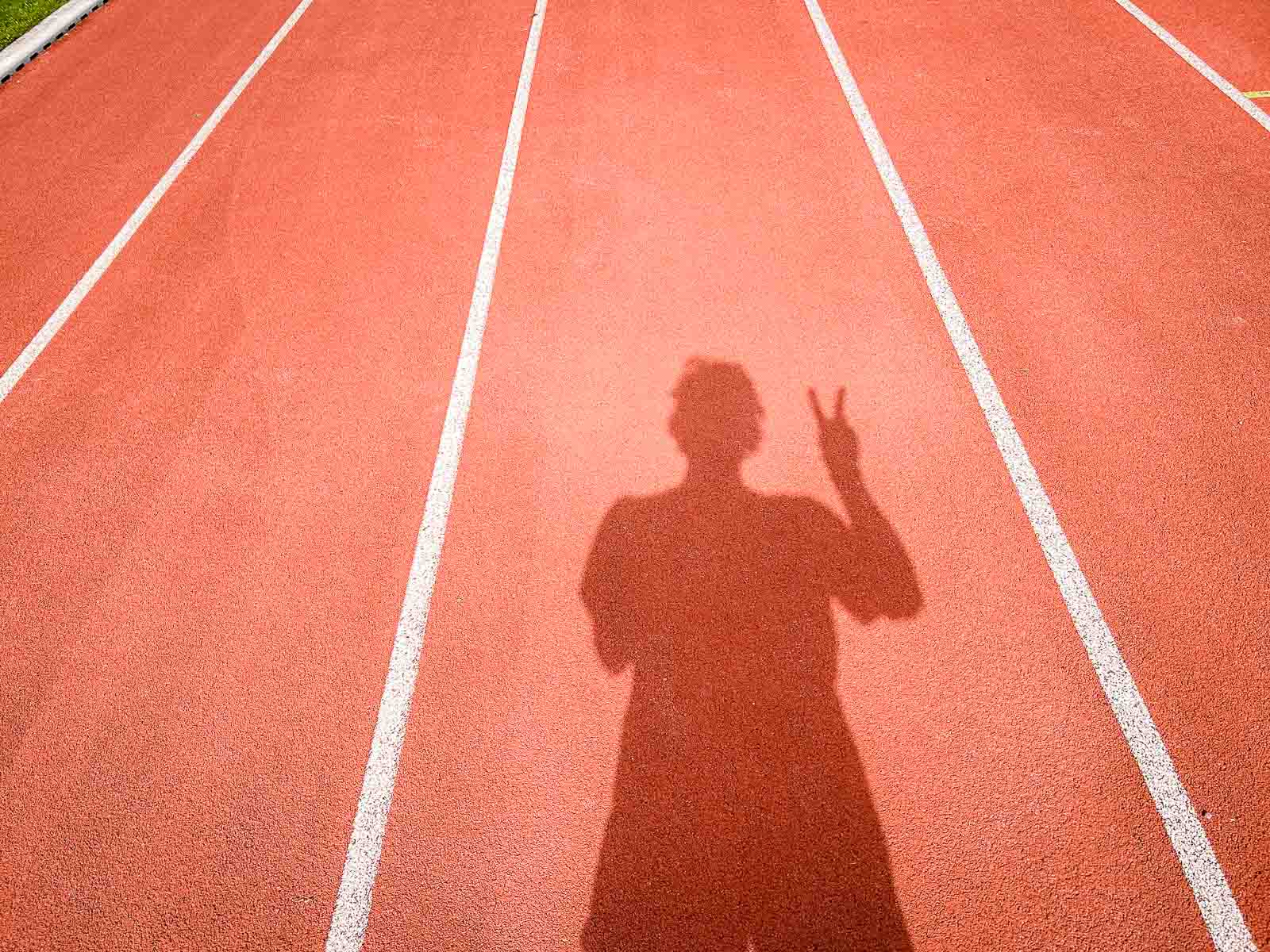 The shadow of a runner on a red track showing the victory sign with their hand. The scene symbolizes success and achievement in running training.
