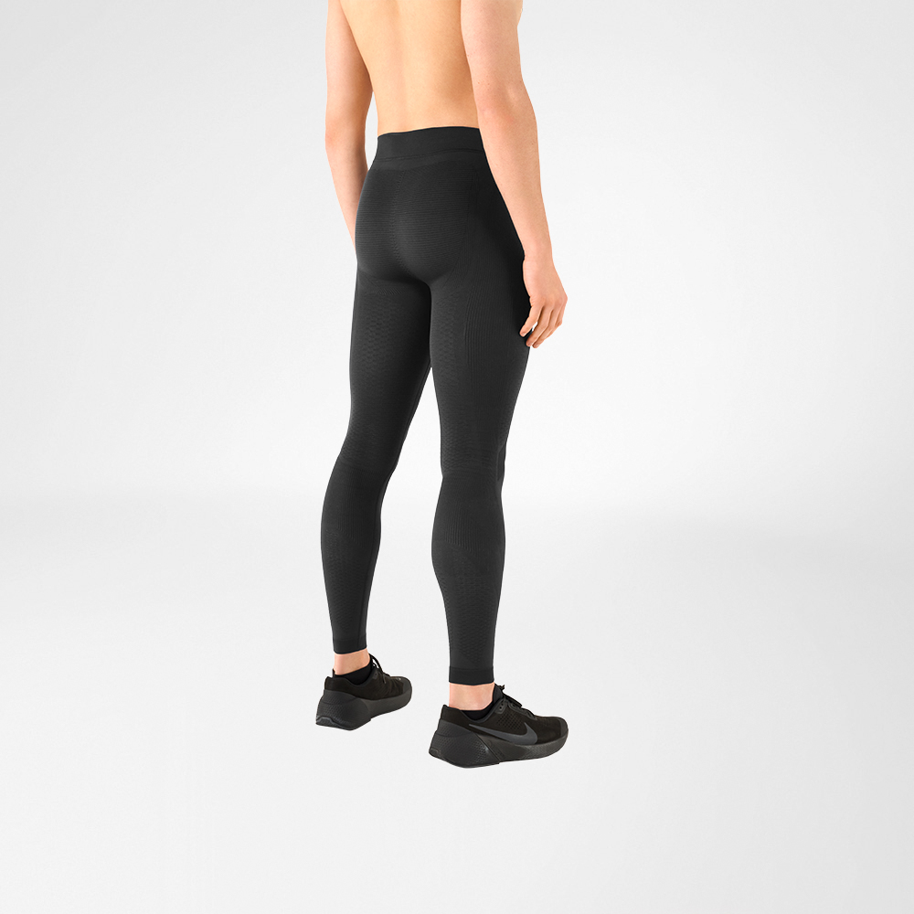 You can see a detail of a shirtless man wearing black sports shoes and anthracite grey compression trousers. He is standing sideways with his back to the camera