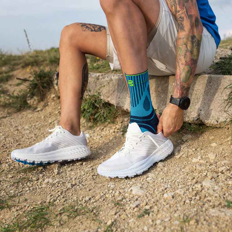 Man pulls a running shoe on a stone on a stone over his Achilles tendon bandage