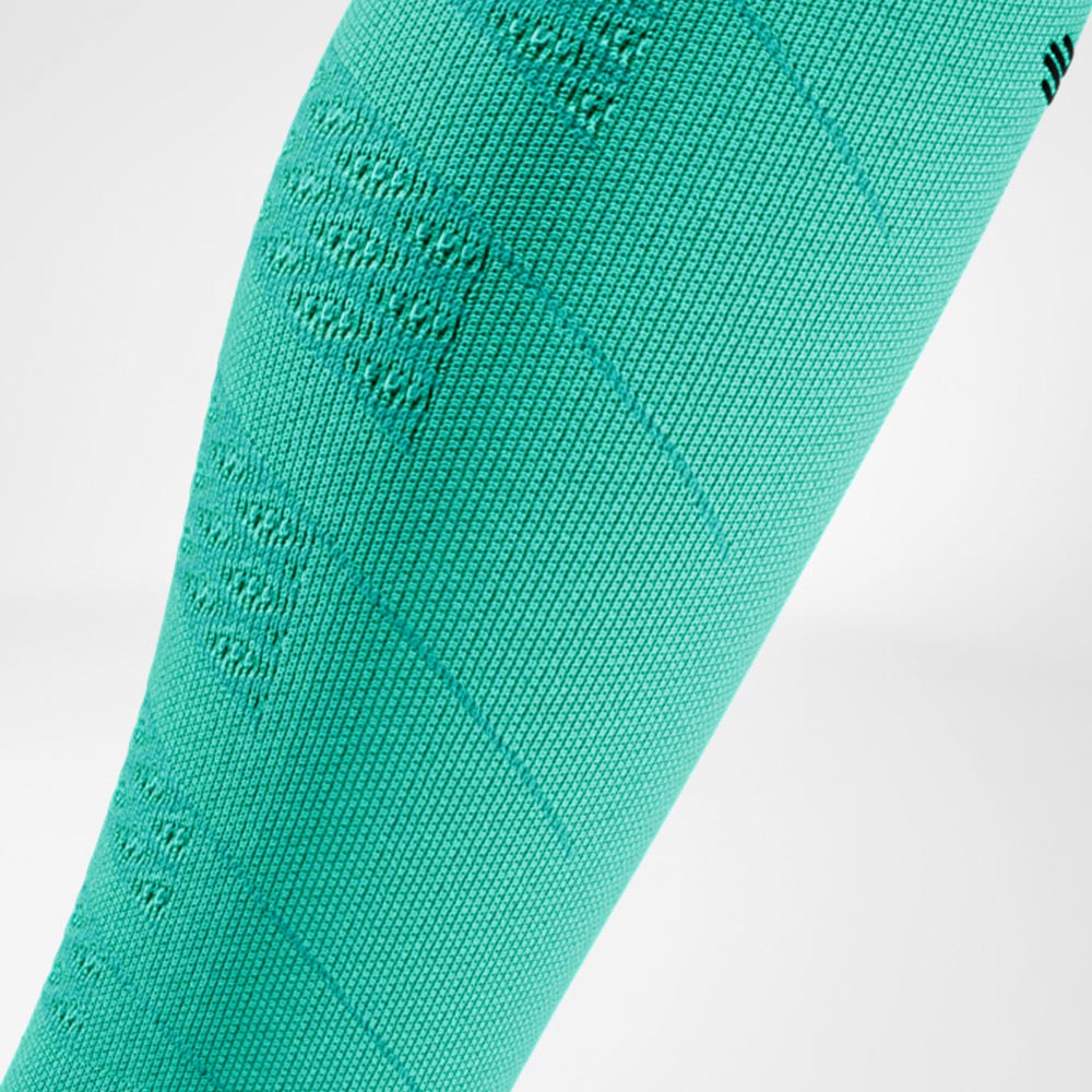 Detail shot of a green Run Performance Compression Sleeve on the lower leg, highlighting the visible knit structure for consistent compression and support during sports activity.