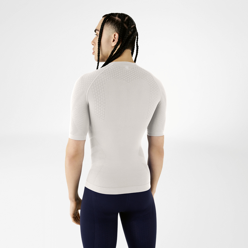 A man wearing a silver-grey compression shirt stands with his back to the camera, looking over his shoulder.