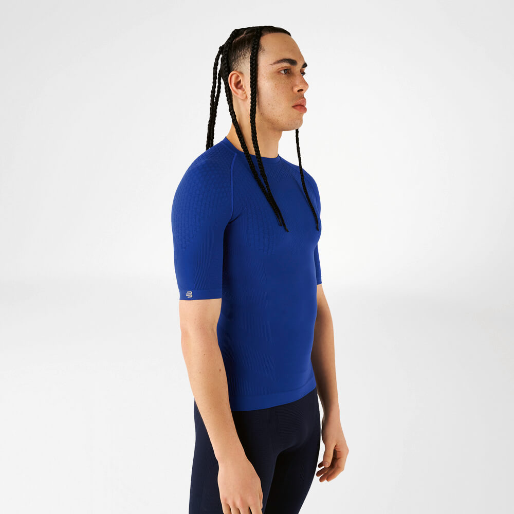 A man wearing a blue compression shirt standing sideways and looking forward.