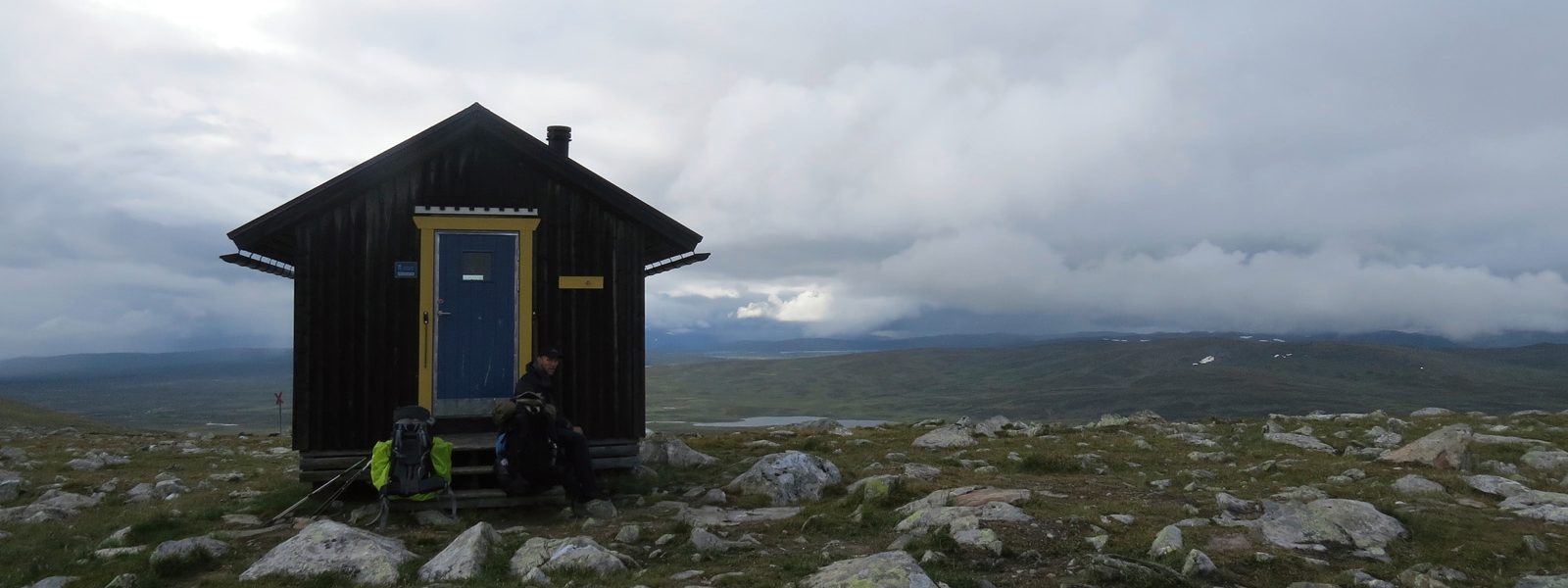 A lonely hut in the mountains in the middle of groving meadows with small rocks in the background the dense cloud cover and a small mountain lake