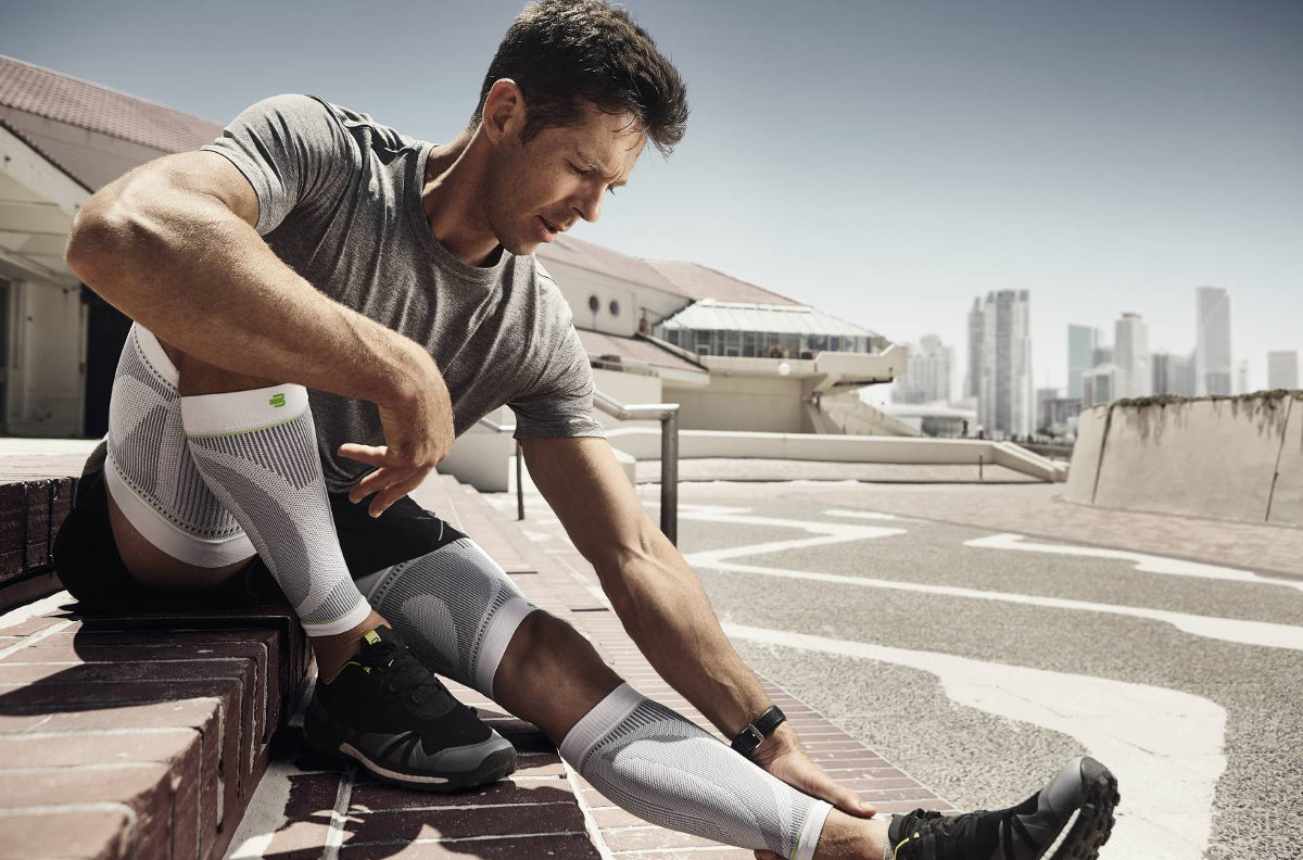 Man rests on stages in the urban environment and wears white upper and lower legs-sleeves