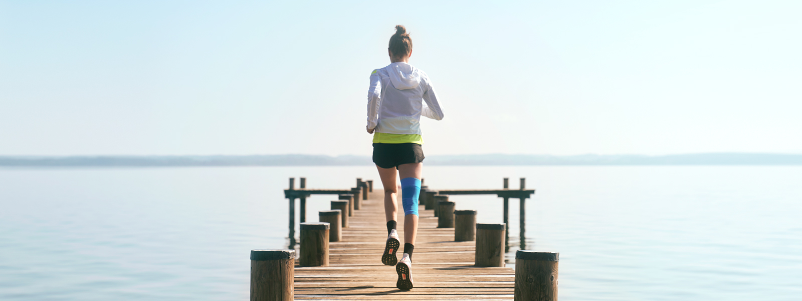 Anna Hahner runs with her Sports Compression Knee Support via a jetty towards the lake