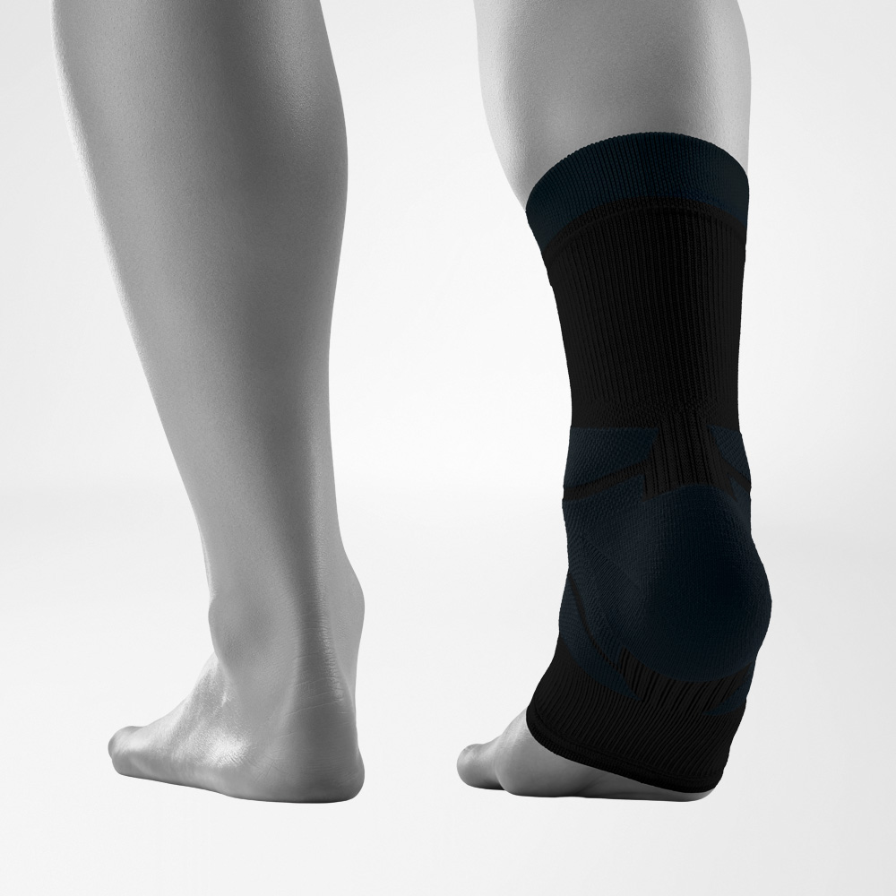 Rear view of both feet against a neutral background, with one foot wearing the black Outdoor Compression Ankle Support. The ankle support fits snugly around the ankle and features different knitted zones designed to provide stability.