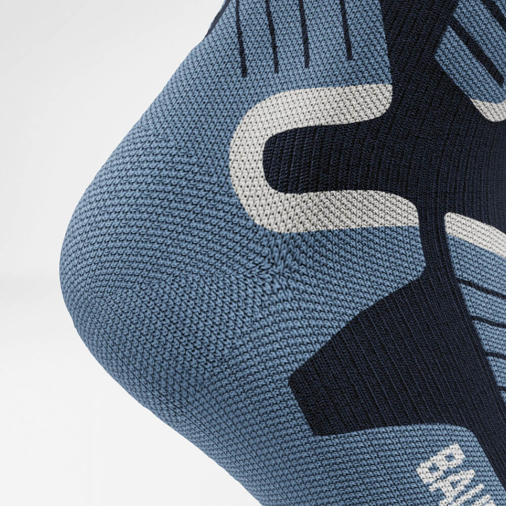 Close-up of the heel of a blue ski compression sock with detailed, breathable knit pattern. The socks provide support and protection for long days of winter sports.