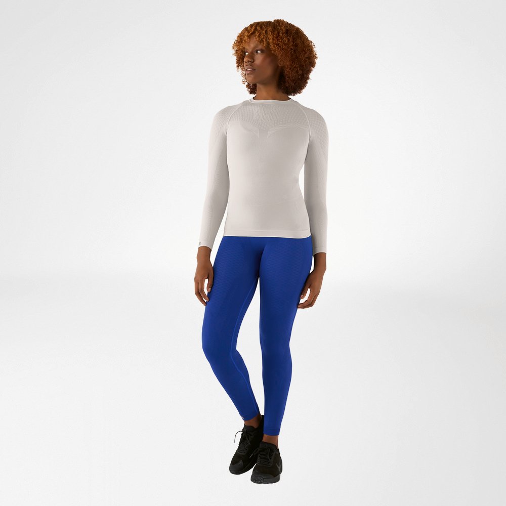 Woman in a silver-grey, close-fitting long sleeve shirt and blue compression pants, front view
