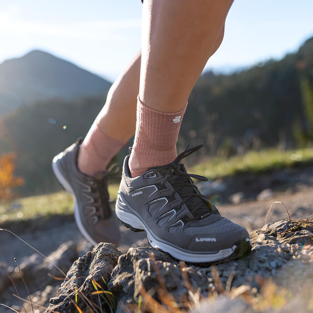Woman wearing Merino Outdoor Socks in coral color during a mountain hike. The socks adapt perfectly to the foot and provide breathability and comfort for long journeys.