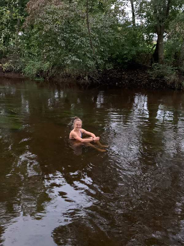 Anna Hahner in the river, surrounded by trees, smiling and looking at the camera.