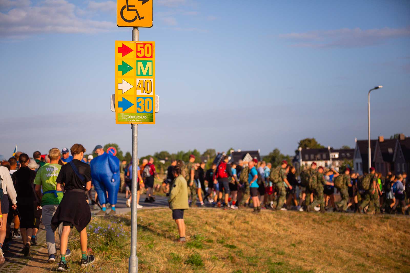 Signpost with colorful arrows marking the 30, 40, and 50 km routes of the 4Daagse, with hikers walking in the background.