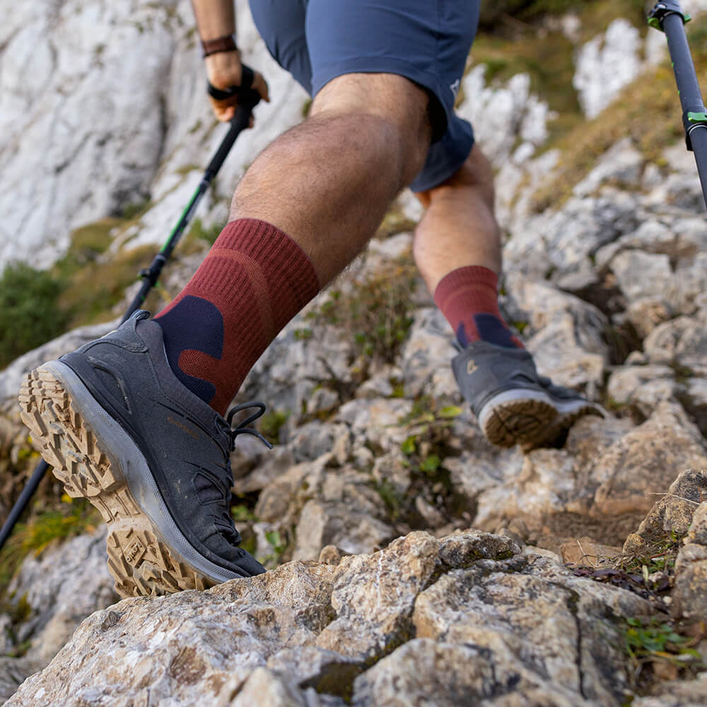 Close-up of a hiker wearing Merino Outdoor Socks in garnet color while climbing a rocky trail. The socks provide support and comfort on challenging terrain.