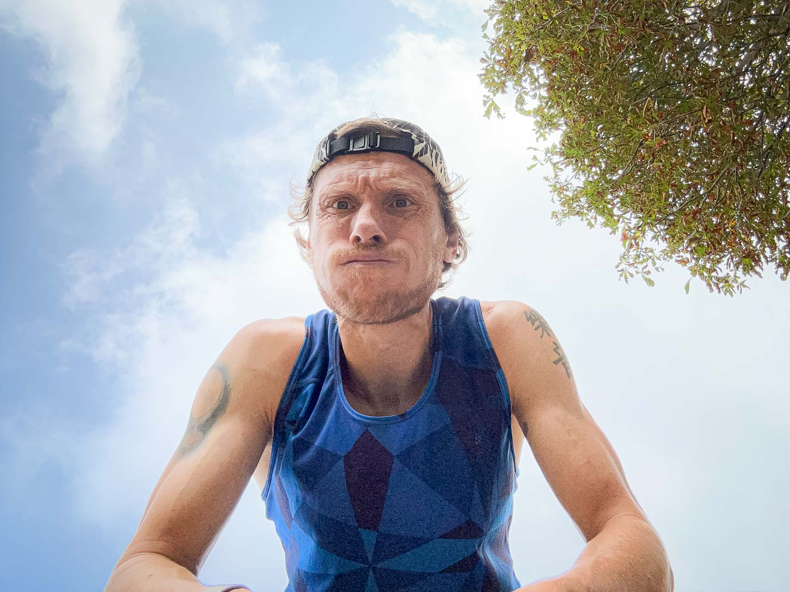 Close-up of a runner breathing heavily after a run. He is wearing a blue singlet and a cap, looking into the camera.