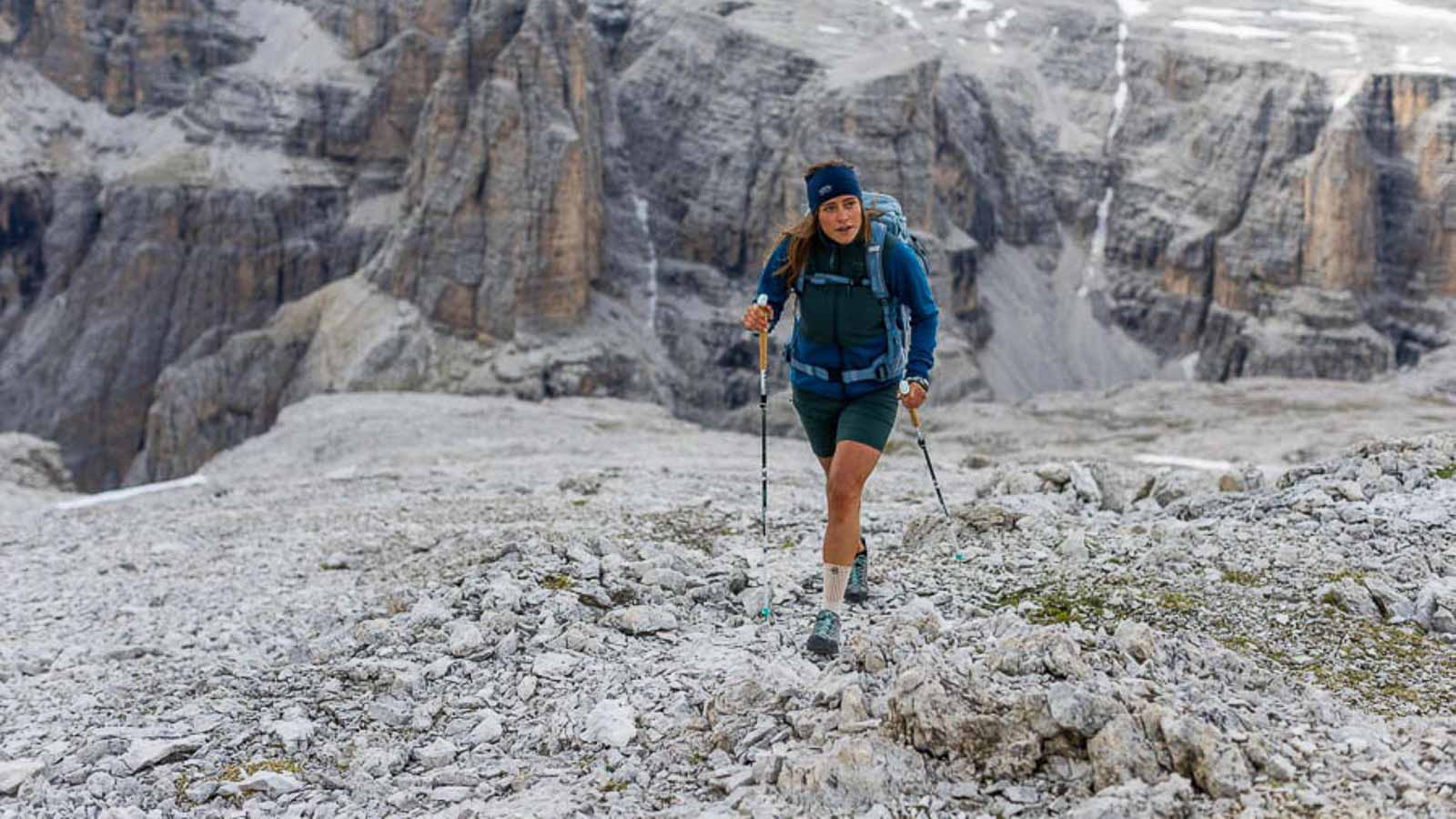A hiker in the Dolomites walks with poles over a rocky field and wears a hiking bandage.
