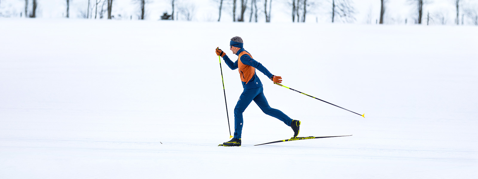 A man in orange and blue clothing is cross-country skiing through the snow.