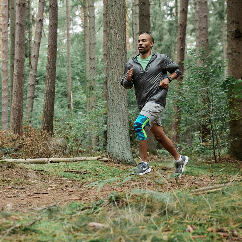 Runner in the forest with a knee bandage A runner dynamically runs through the forest wearing a knee bandage