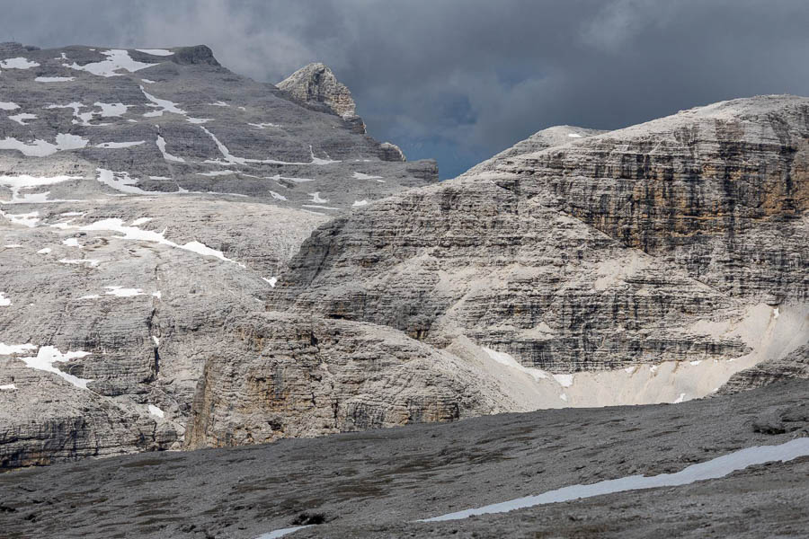 A rocky landscape in the Dolomites with scattered patches of snow and a cloudy sky.
