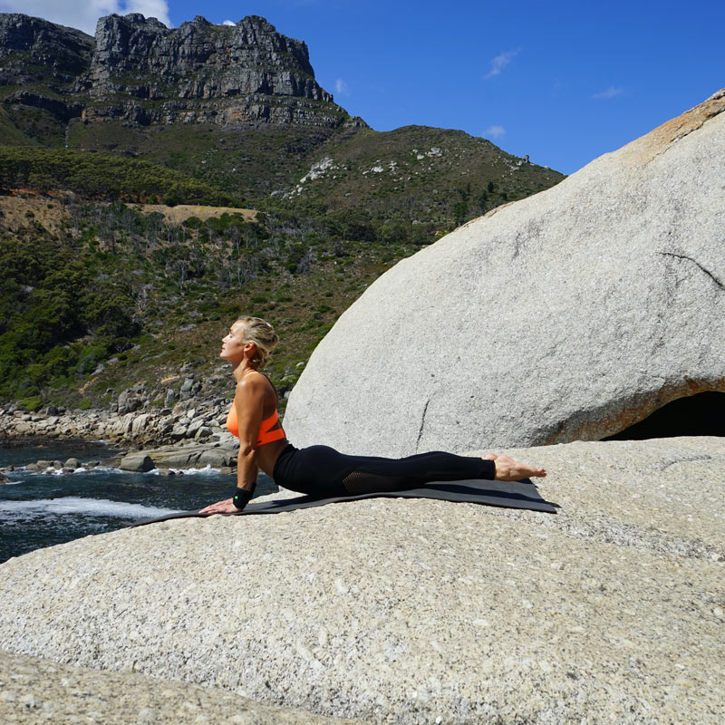 Woman with wrist bandage on rocks in the King Cobra pose supports her palms on the legs straight on the floor