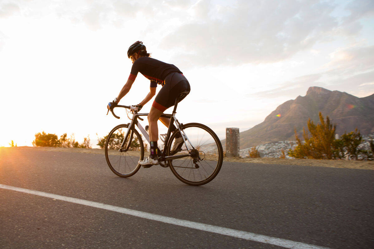 Woman runs on a racing bike on a street towards sunset