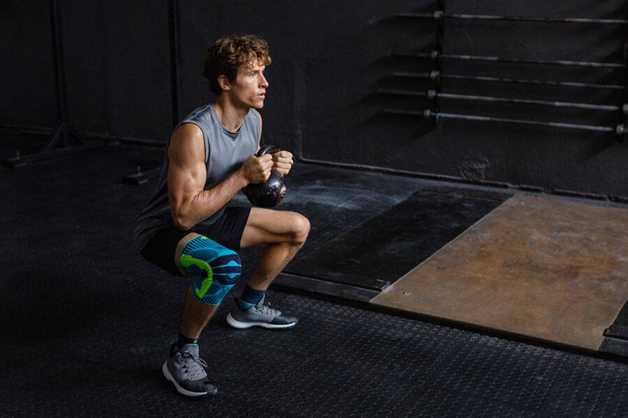 Man with a kneeboard goes deeply crouched with a kettlebell between the two hands
