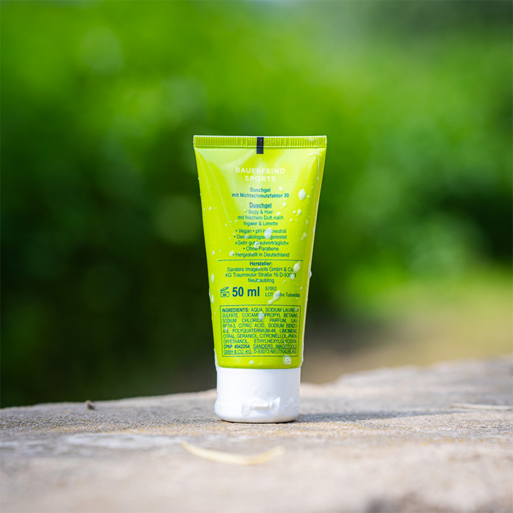 Back view of the green Bauerfeind Sports "ShowerPower" shower gel tube with ingredients and product information. The tube stands on a rock outdoors.