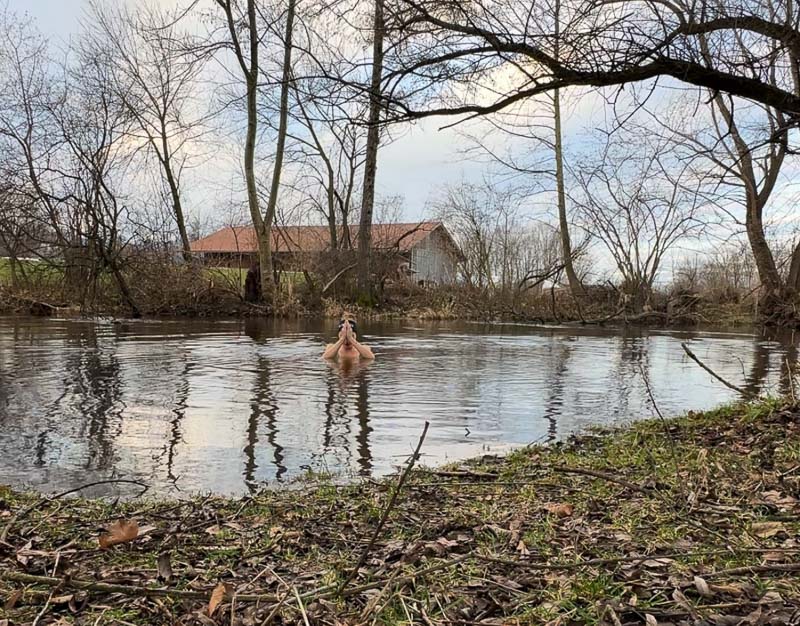 Anna Hahner praying with folded hands in the river, surrounded by bare trees.