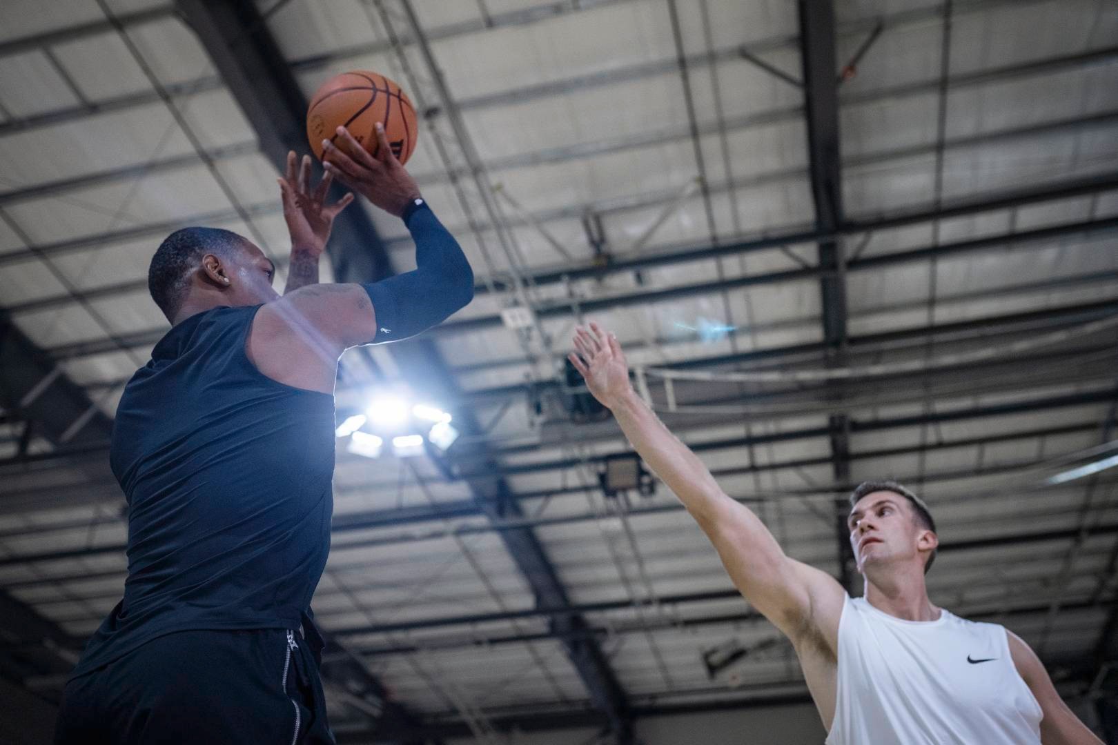 Basketball players with a blue armsleeve in sports hall tries to throw over the outstretched arm of an opposite