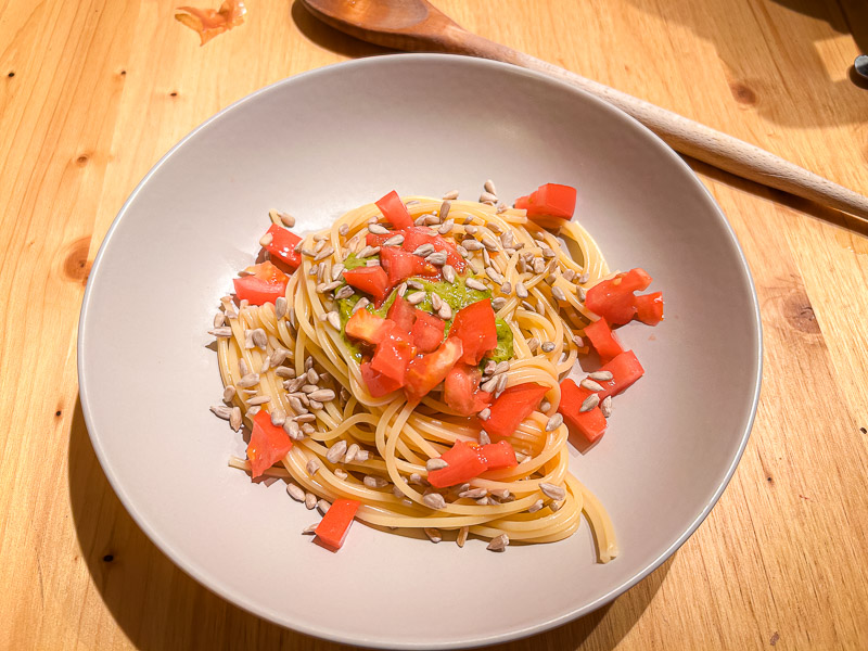 A plate of spaghetti with fresh tomatoes and sunflower seeds, perfect for a carbohydrate-rich meal before a half marathon.