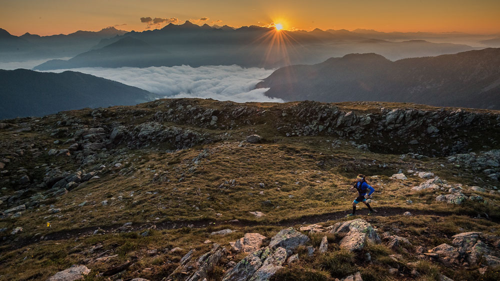 Ultra runner on a mountain trail at sunrise overlooking the Alps