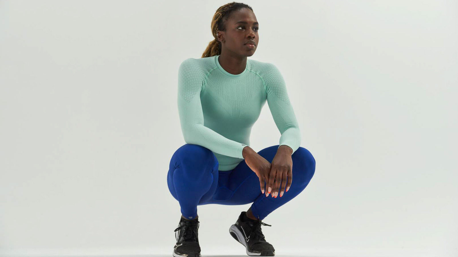 Athlete in mint green compression shirt and blue compression pants Athlete in mint green compression shirt and blue compression pants in a squat position in front of a white background.