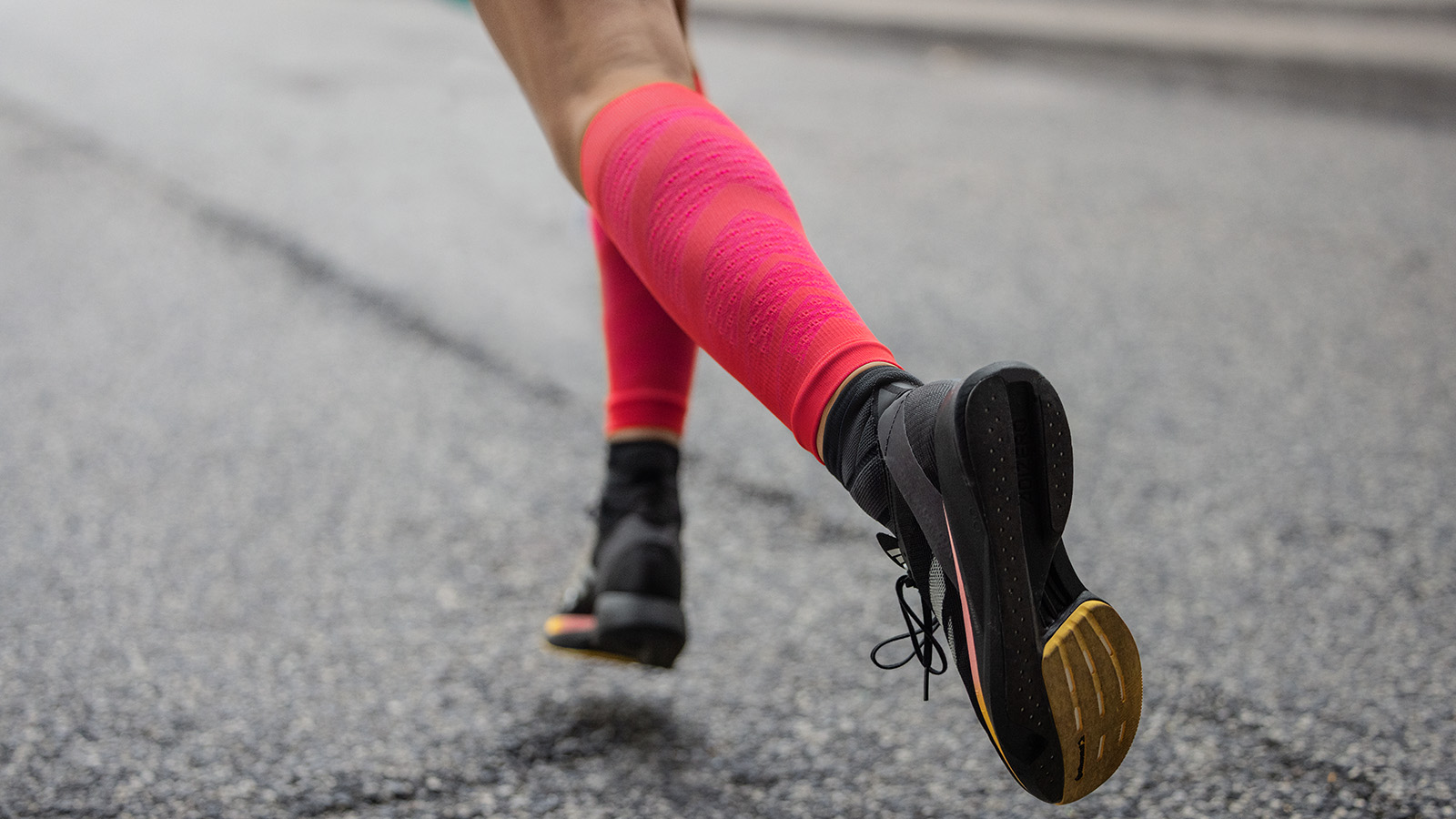 Close up: long pink running socks and black running shoes run over a paved road in a city