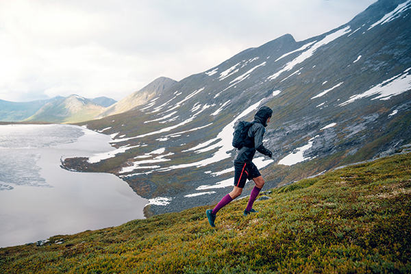 Trailrunner runs a grassy mountain up in rainy weather