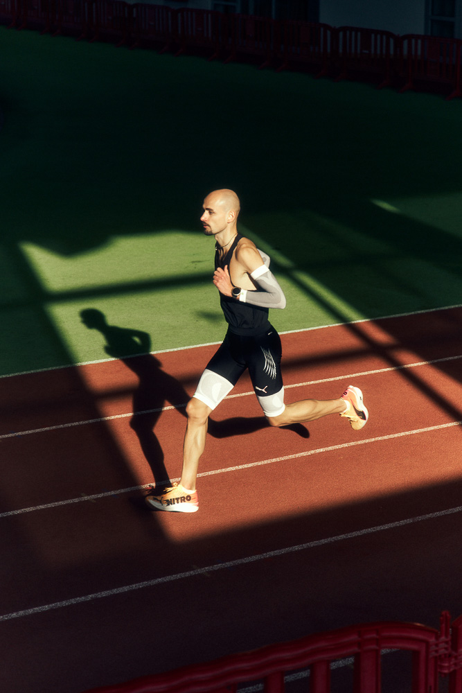 Professional runner Hendrik Pfeiffer sprints on an indoor track, supported by compression sleeves on arms and legs for stability and performance.
