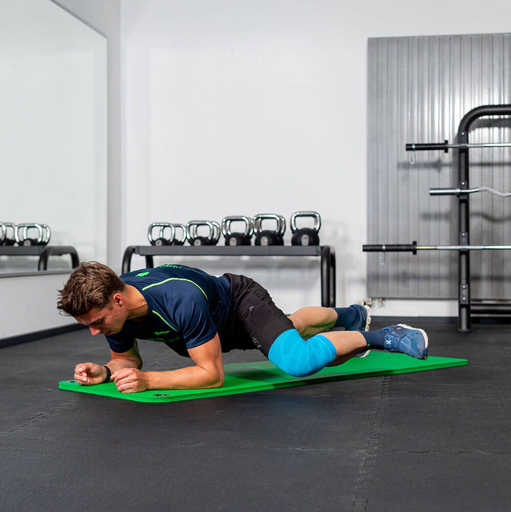Man in the gym moves his left knee forward at a forearm Plank