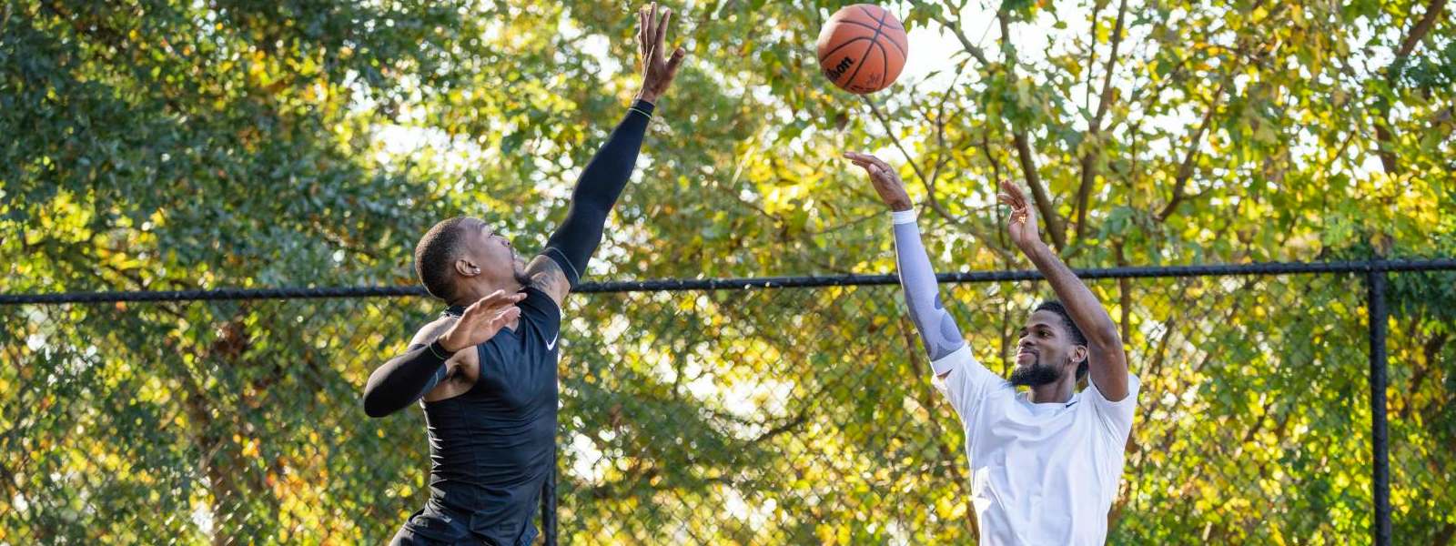 Basketball players in black game clothing tries to block his opponent in white clothes high above the ground