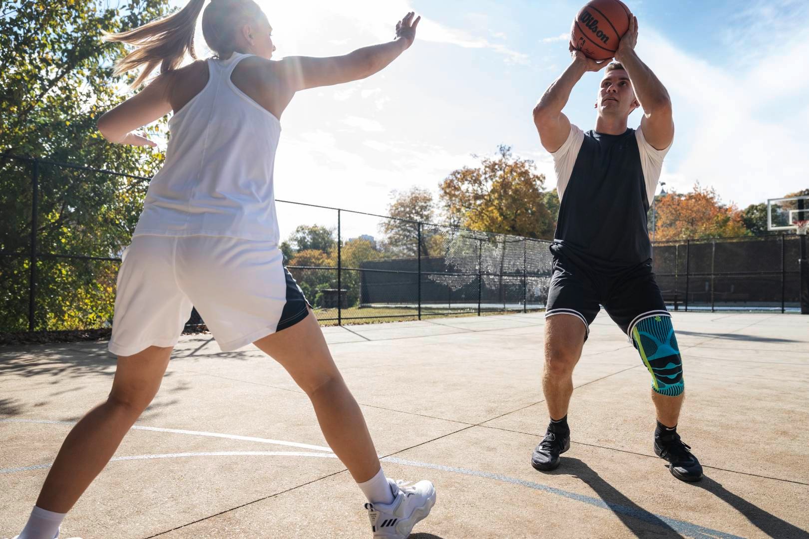 Basketball players with a kneeze starts with a streetball while his opponent tries to block him