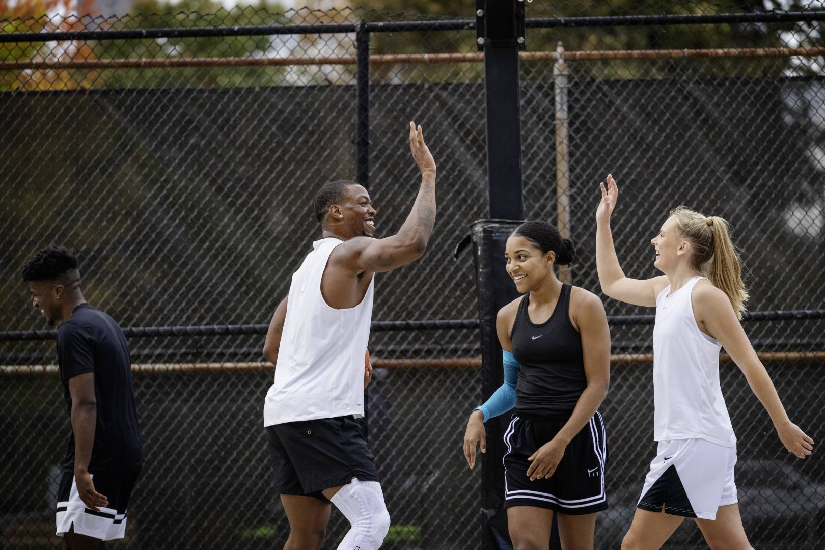 Two basketball players in white game clothes clap cheerfully while their opponents in black look into different directions in black