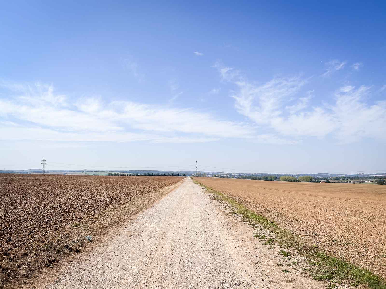 A long, straight gravel path stretching through a vast landscape with clear skies and fields on both sides. Ideal running route for endurance runs.