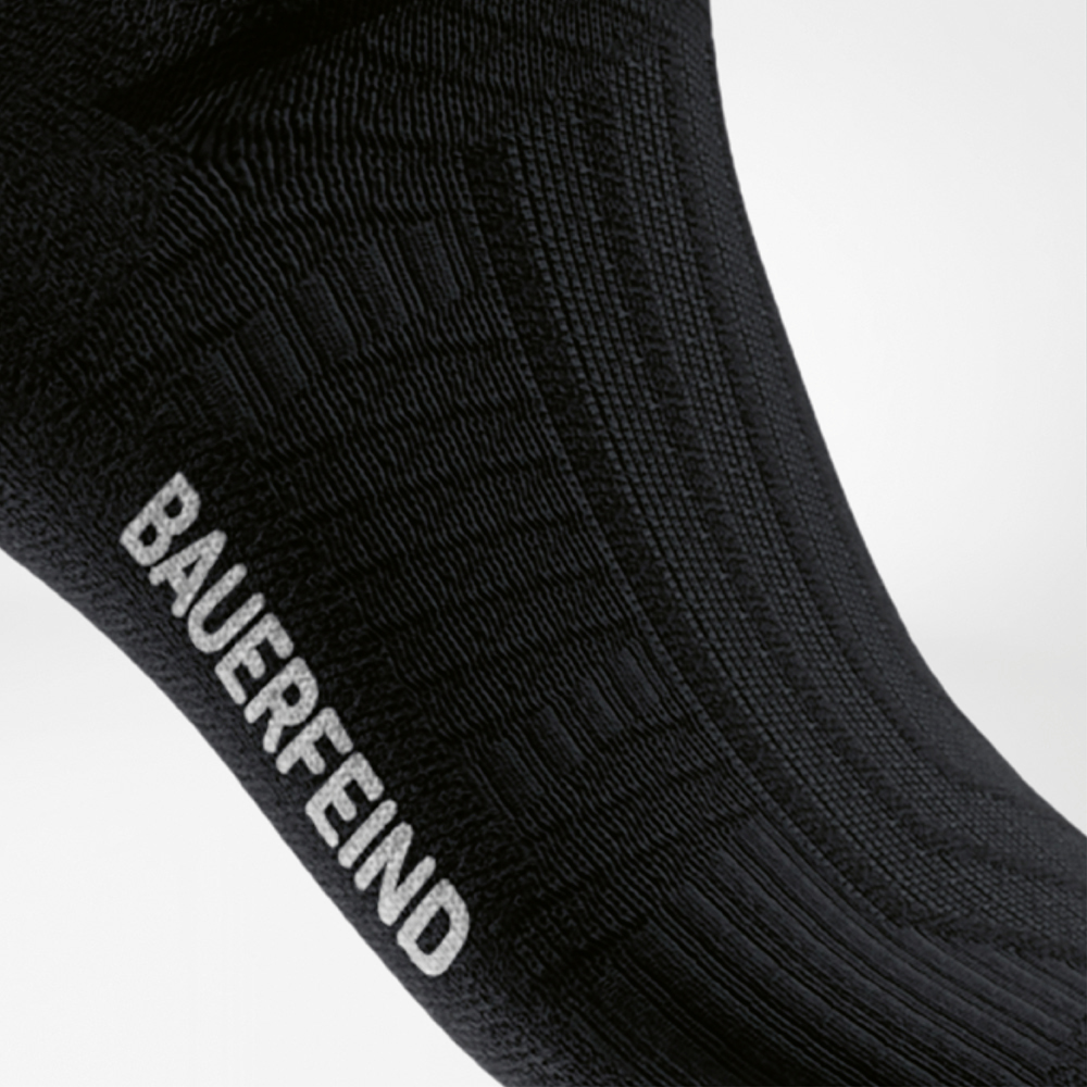 Stable with every step – Performance grip meets BAUERFEIND quality Close-up of the instep area of a black compression running sock with knitted BAUERFEIND logo and textured surface for optimal grip.