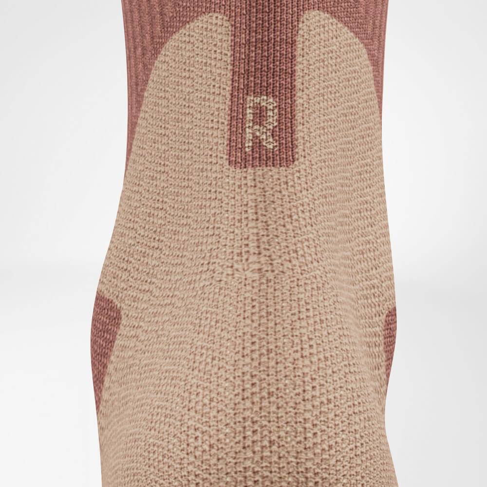 Close-up of the Achilles area of an outdoor sock in coral and gray. The detailed knit structure highlights the comfort zone in the heel area.