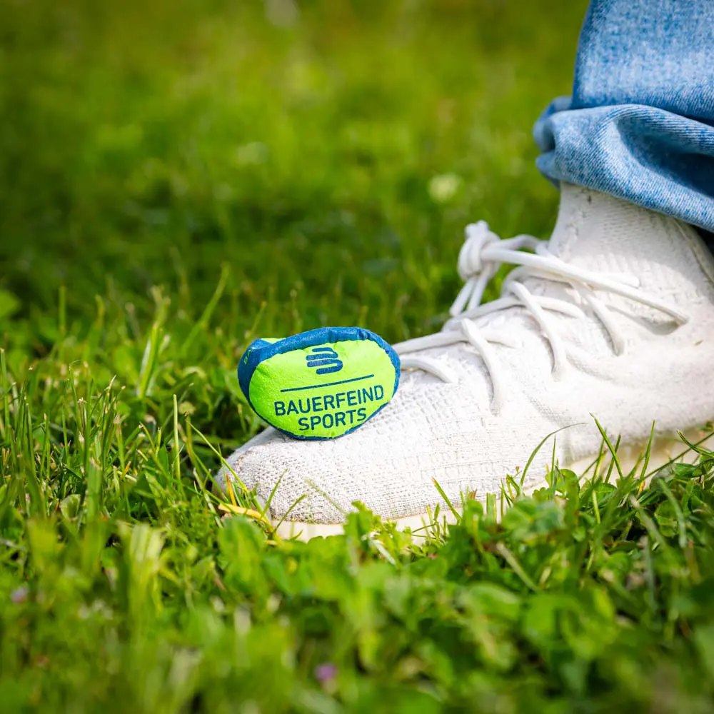 Small Bauerfeind Sports ball on grass, placed next to a white shoe.