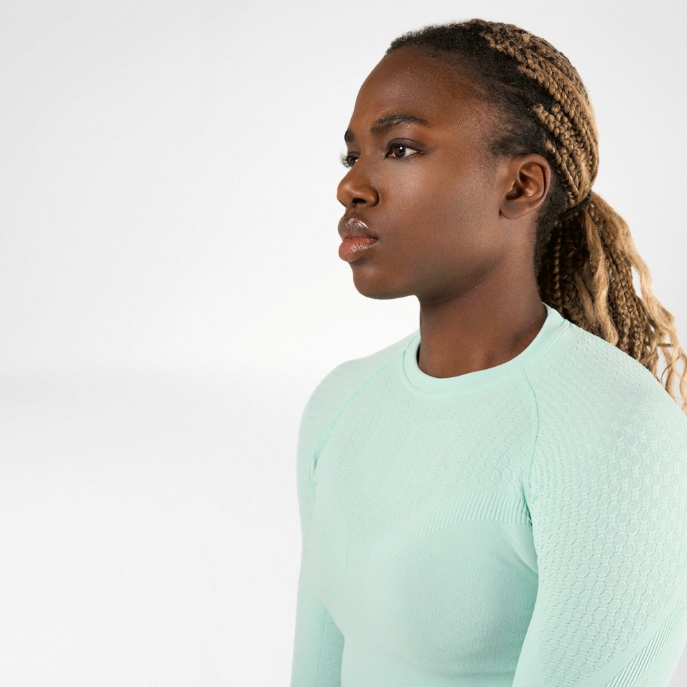 A sporty woman with braided hair wearing a light green, long-sleeved compression shirt is viewed from the side. She has a focused and determined expression on her face.