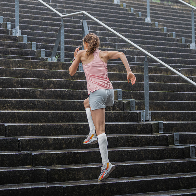 Woman runs through a city with her feet in the air and wears white running socks