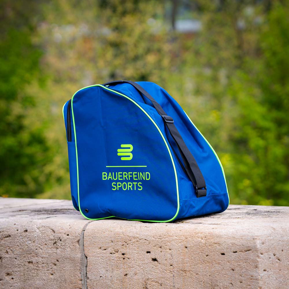 A blue bag with the Bauerfeind Sports logo, photographed outdoors on a stone background. The bag features green accents and black straps.