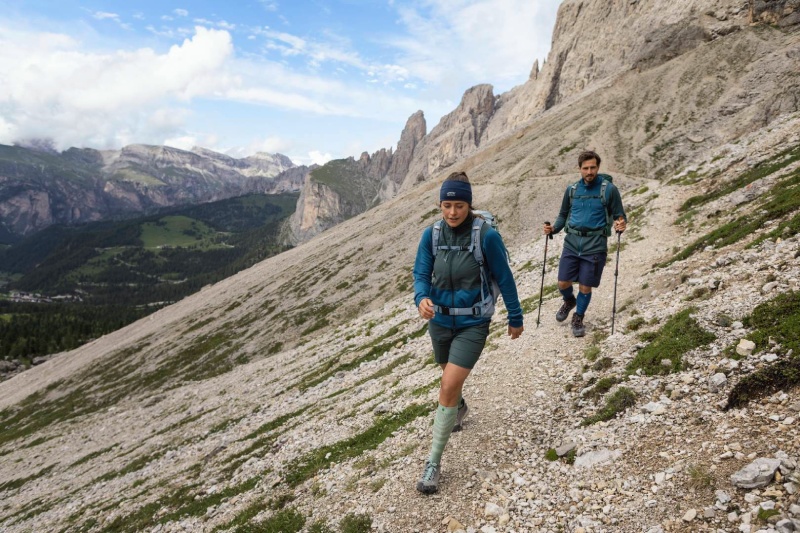 A woman and a man hike on a mountain range surrounded by rocks and wear backpack telescopic sticks and long hiking socks
