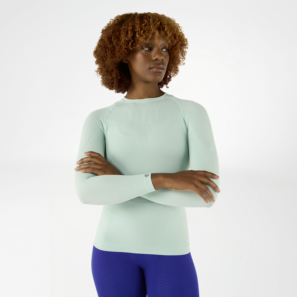 Woman in a light green, close-fitting long sleeve shirt with crossed arms, front view
